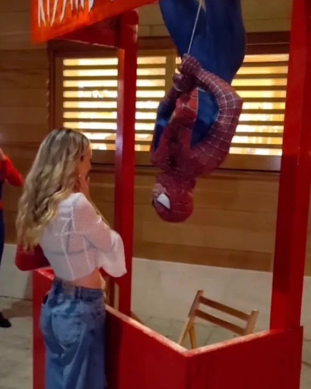 A woman reacting at a red kissing booth where Spider-Man hangs upside down